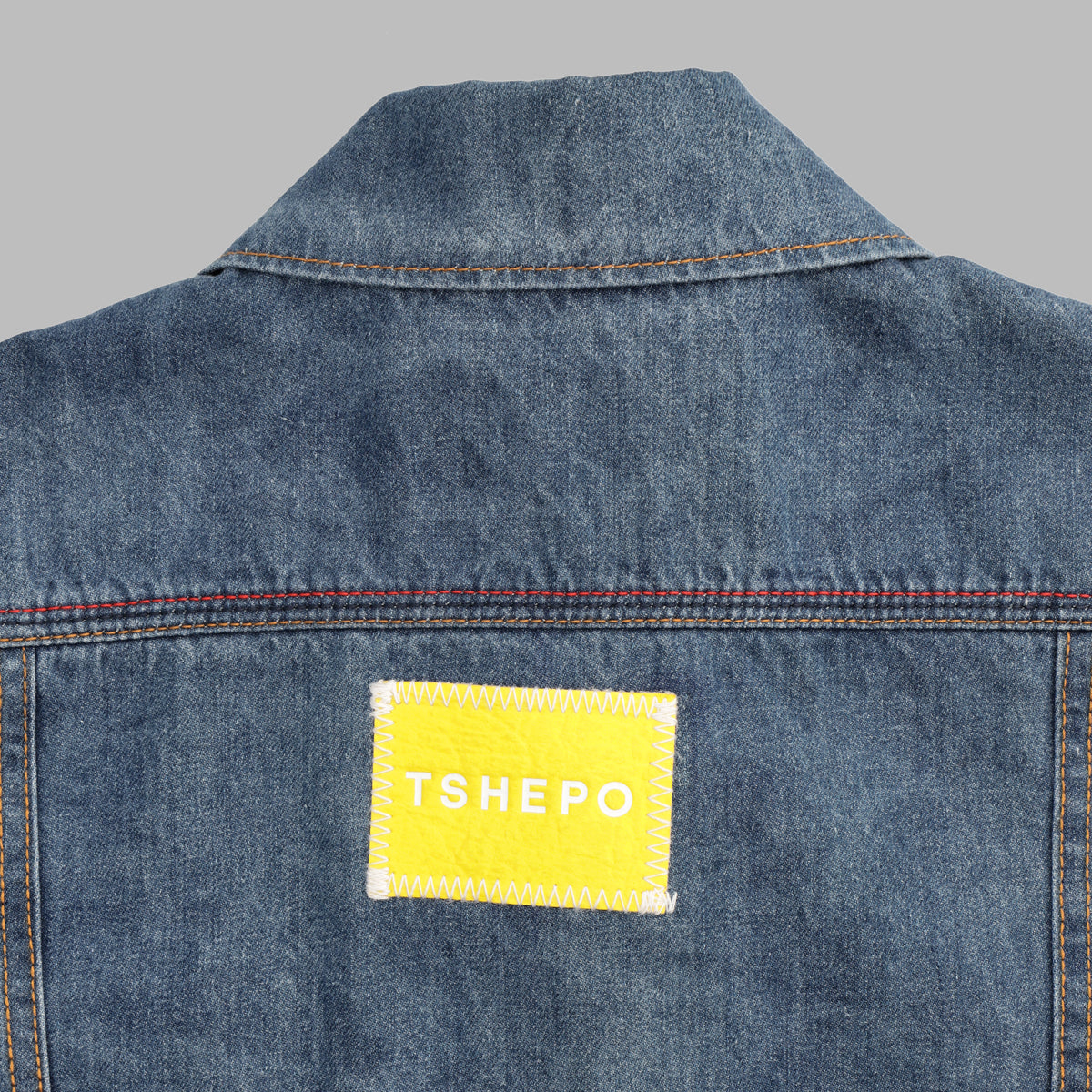 The back of a light wash TSHEPO trucker jacket with a yellow leather stitch